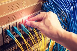man working in network server room with Fiber Optic cables connected to optic ports and UTP